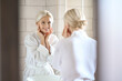 © insta_photos - Gorgeous mid age adult 50 years old blonde woman standing in bathroom wearing bathrobe touching face, looking at reflection in mirror smiling doing morning beauty routine. Antiage skin care concept.