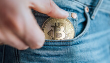 Close Up Footage Of Man's Fingers Putting The Bitcoin Coin In The Blue Jeans Small Pocket. Savings, Digital Currency, Cryptocurrency, Investing, And Smart Outgoings Managing Concept.