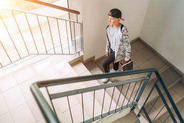 Teenager skateboarder boy with a skateboard going up by staircase home. Youth generation Freetime spending concept image.