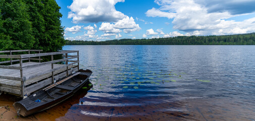 Wall Mural - calm blue lake in the middle of the forest with a wooden dock and rowboat in the foreground