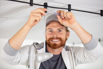 Wall Mural - handsome male electrician changing the light bulb