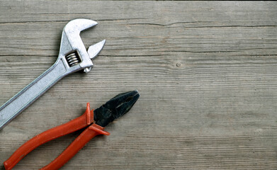 Pliers with red handles, adjustable wrench on an old wooden background. Flat Lay