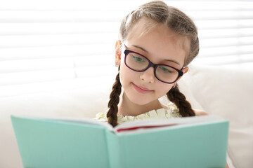 Wall Mural - Cute little girl reading book near window at home