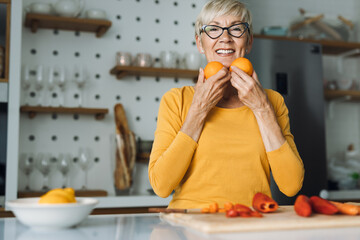 Happy senior woman holding oranges in the kitchen and looking at camera