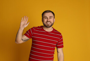 Wall Mural - Happy young man waving to say hello on yellow background