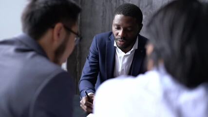 Wall Mural - Handsome african american businessman talking in negotiations with asian partners sitting at the table