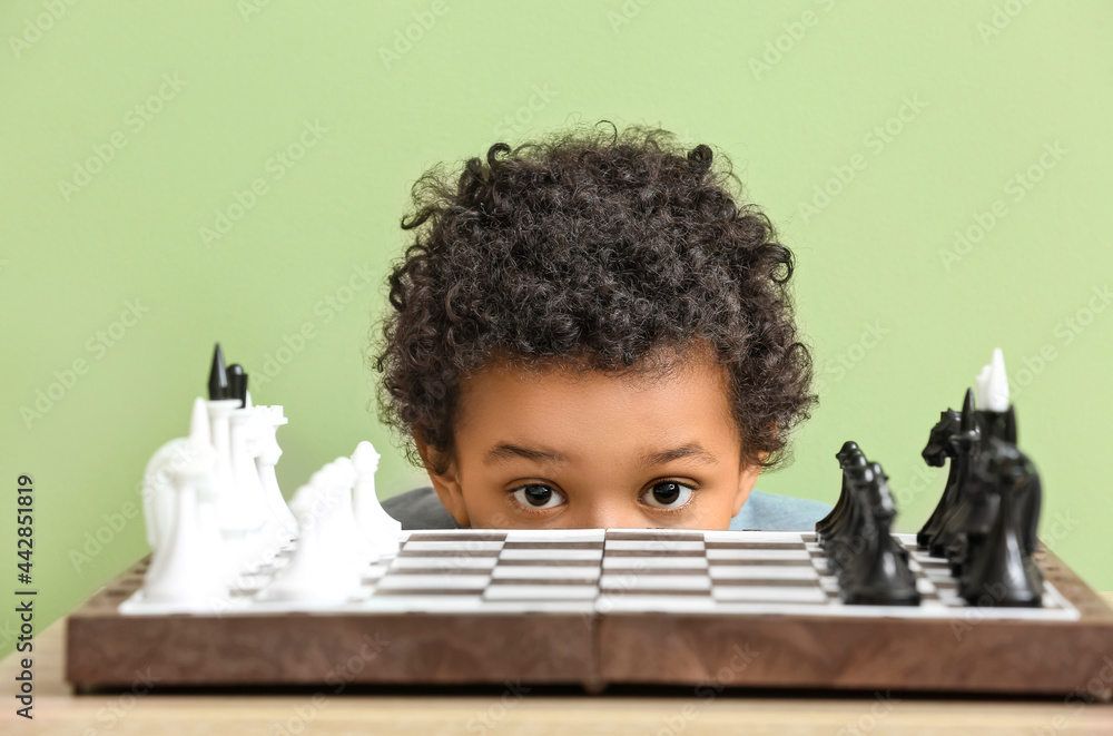 Cute African-American boy playing chess on color background