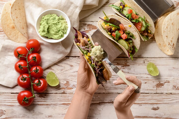 Wall Mural - Female hands with taco and tasty guacamole on light wooden background