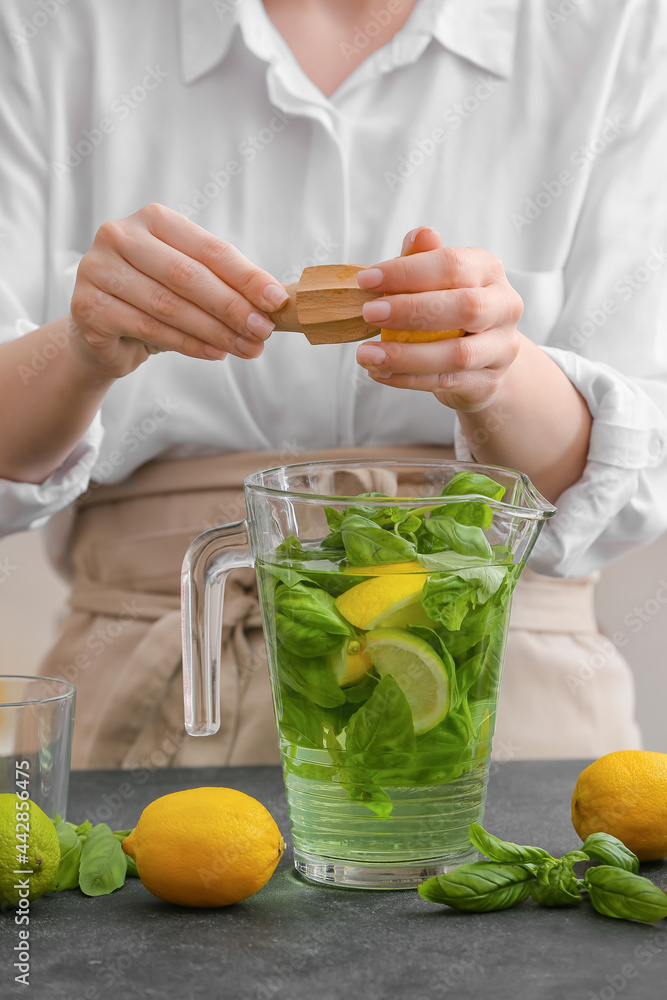 Woman making lemonade with basil on table in kitchen