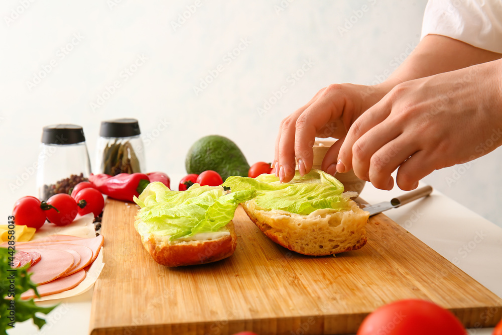 Woman preparing tasty sandwiches on light background
