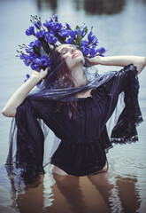 Beautiful girl in wreath of flowers at lake. Portrait of Young beautiful woman. Young pagan girl conduct ceremony on Midsummer. Earth Day