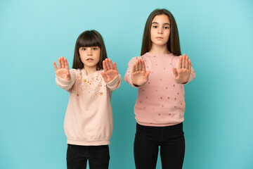 Canvas Print - Little sisters girls isolated on blue background making stop gesture for disappointed with an opinion