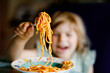 © Irina Schmidt - Adorable toddler girl eat pasta spaghetti with tomato bolognese with minced meat. Happy preschool child eating fresh cooked healthy meal with noodles and vegetables at home, indoors.