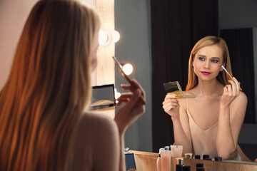 Wall Mural - Beautiful woman applying makeup near mirror in room