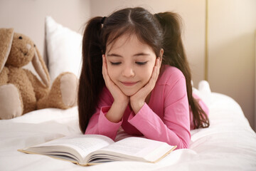 Sticker - Little girl reading book on bed at home