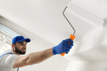 Wall Mural - Handyman painting ceiling with white dye indoors, focus on roller