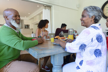 Wall Mural - Happy african american multi generation family sitting at table smiling during breakfast