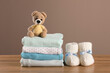 Stack of baby boy's clothes, booties and toy on wooden table against brown background, space for text