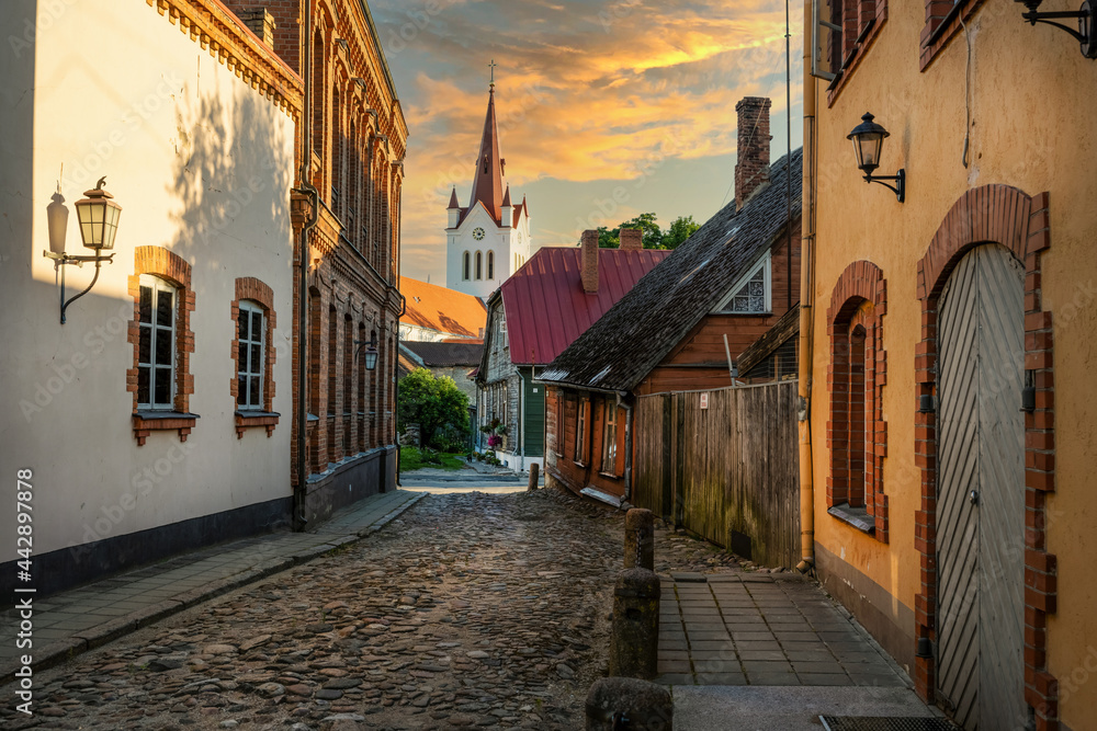 sunset view to the St. John’s church tower from small street with old architecture in town Cesis, Latvia - obrazy, fototapety, plakaty 