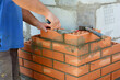Masonry brickwork. A masonry contractor is laying the house corner with face bricks bonding them with a concrete block wall with a wire mesh using a trowel, mortar and a hammer.