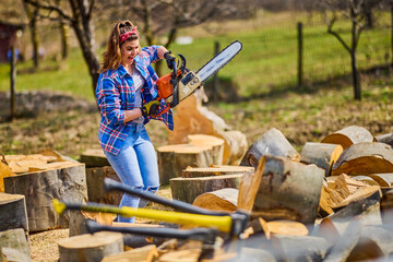 Wall Mural - Young Woman using chainsaw to cut a log for firewood.