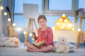 Wall Mural - Little girl reading book with flashlight in evening room