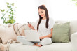 © deagreez - Photo of positive confident lady look pc screen hold debit card wear white t-shirt sit sofa in room indoors