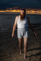 Wall Mural - A humorous portrait of a brutal man in a T-shirt and boxers on the beach at sunset