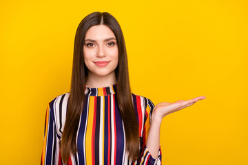 Wall Mural - Photo portrait pretty girl smiling keeping empty space on palm isolated vibrant yellow color background