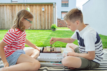 Wall Mural - Happy children playing chess on backyard at sunny day while summer holidays