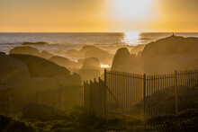 Sunset At Camps Bay. During Golden Hour, The Mist And The Waves Allow Sun Rays To Be Appreciated And Behind A Fence. Cape Town, South Africa, Cape Of Good Hope.