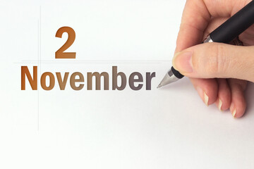 November 2nd. Day 2 of month, Calendar date. The hand holds a black pen and writes the calendar date. Autumn month, day of the year concept.