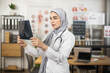 © sofiko14 - Qualified female doctor analysing x ray prints while standing at her cabinet. Young woman in hijab and white lab coat working with scan of severe patient.