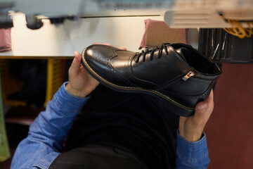 Man holding black leather boot. Close up shot from above of new stylish footwear in hands of shoe factory worker. Concept of shoe manufacturing industry. Top view, closeup