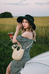 Wall Mural - Beautiful young woman in dress and hat stands.  near a white car.