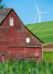 Rustic wooden red barn with modern wind turbines in the background seen from rural farming area 