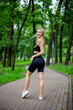 © Hennadii - Young beautiful sporty blonde woman in a black T-shirt and in black tight sports shorts in good shape posing in front of green trees