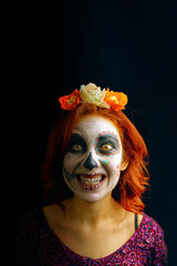 Young woman in day of the dead mask skull face art makeup and red hair showing teeth on dark background crazy smile