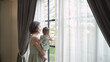 portrait of happy asian woman mother holding baby infant near window looking away at home. 4 months baby embracing in parent arm. relationship mother and daughter. mom carrying baby infant in bedroom