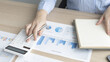 © Puwasit Inyavileart - Head of accounting is recording the company's financial growth statistics using graphs as a reference for reviewing and analyzing the results, Taking notes and analyzing data graphs in office.