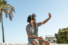 Young Man Having Fun Taking Selfie With Mobile Smartphone While Listening Music With Headphones And Vintage Boombox During Summer Vacations