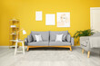 Trendy interior of living room with grey furniture and yellow wall