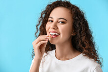 Young Woman Taking Fish Oil Pill On Color Background