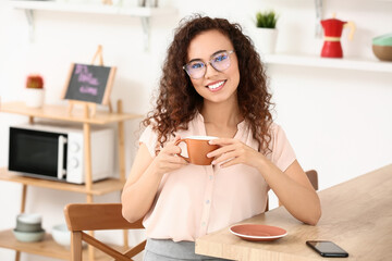 Wall Mural - Beautiful young woman drinking coffee in kitchen