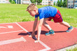 © ARVD73 - Caucasian boy,kid prepare to start running on a red track.young boy in starting position ready for running.Summer day.