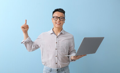 Poster - Portrait of Asian teacher with laptop and raised index finger on color background