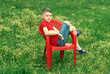 Boy sitting on a red chair in the field