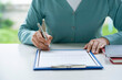 © crizzystudio - Businesswoman signing a document or application form in a folder, Woman signing document with pen on a desk at home