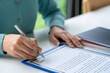 © crizzystudio - Businesswoman signing a document or application form in a folder, Woman signing document with pen on a desk at home