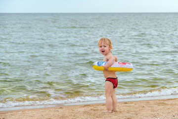 A little girl with an inflatable ring on the seashore invites children to swim and swim in the water.